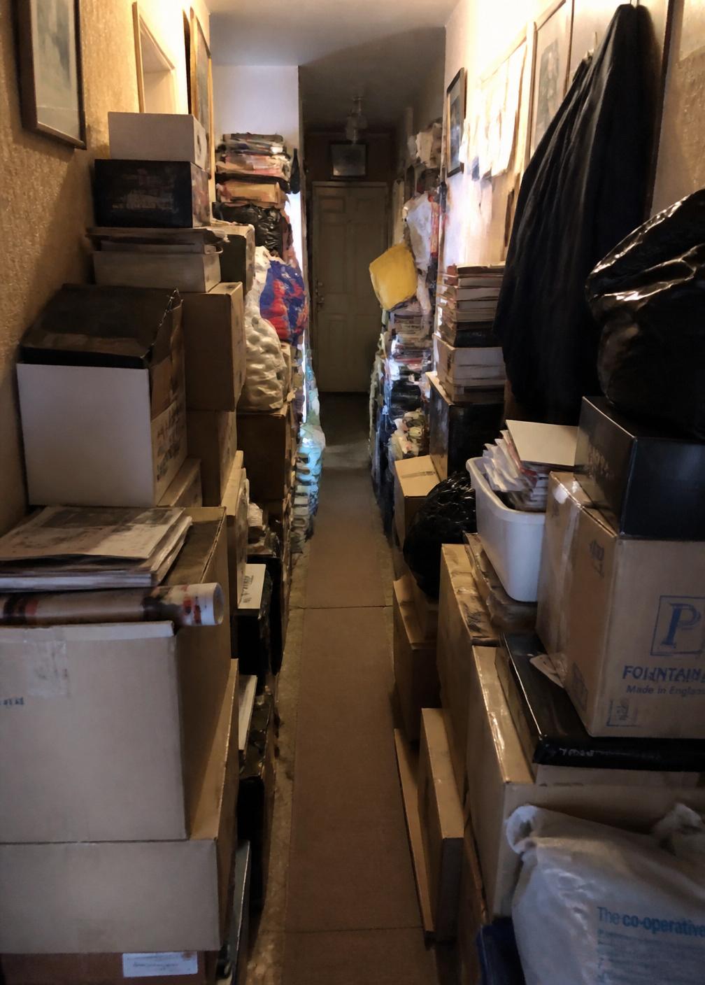Narrow hoarded hallway with boxes stacked shoulder high on both sides